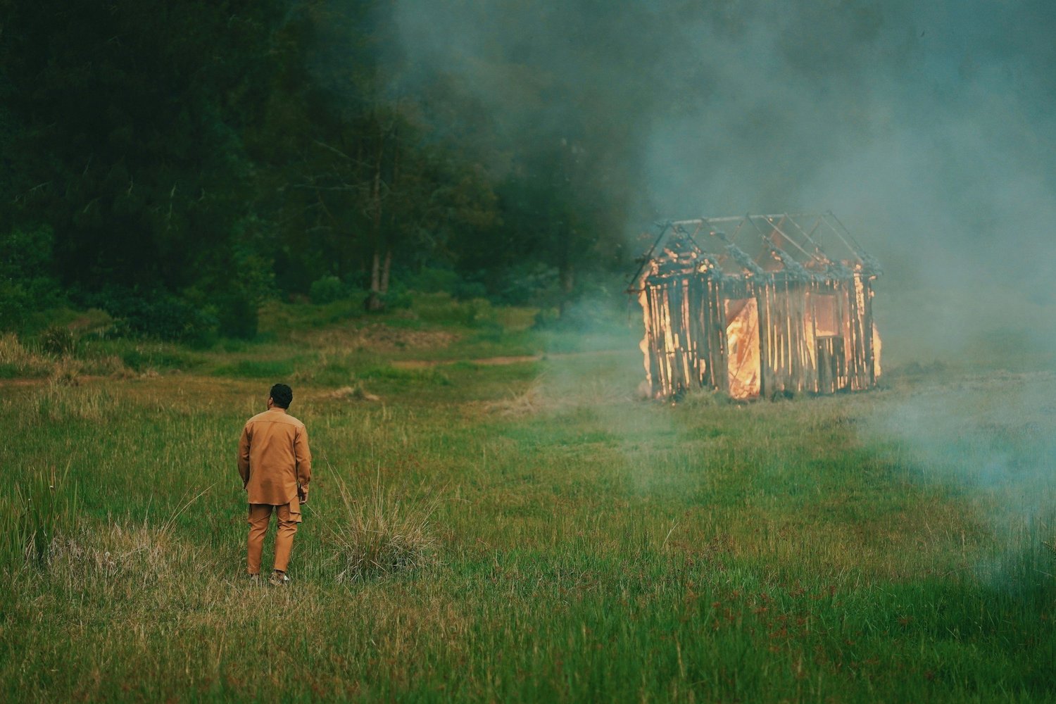 Person walking toward a burning wooden structure in a field